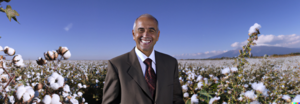 DALL·E 2023-01-08 14.54.03 - perfect face and perfect picture, high-res picture of a North African man, in his sixties, in a suit, in front of a cotton field, clear blue sky with.png